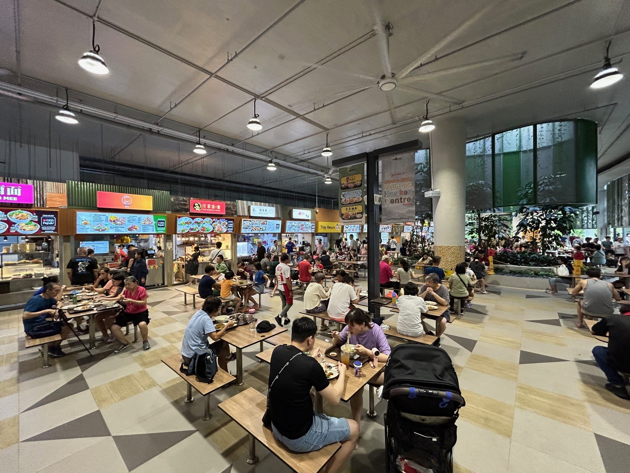 A bustling food center with people eating at tables. Food stalls are visible in the background.